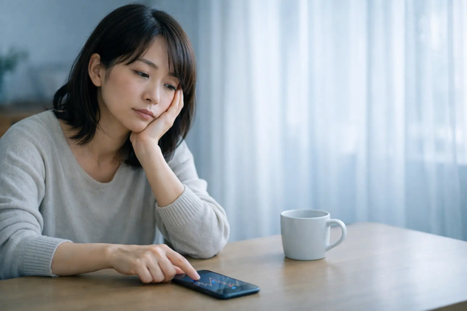 FXをやめたいと悩みながらスマホのチャートを見る30代女性